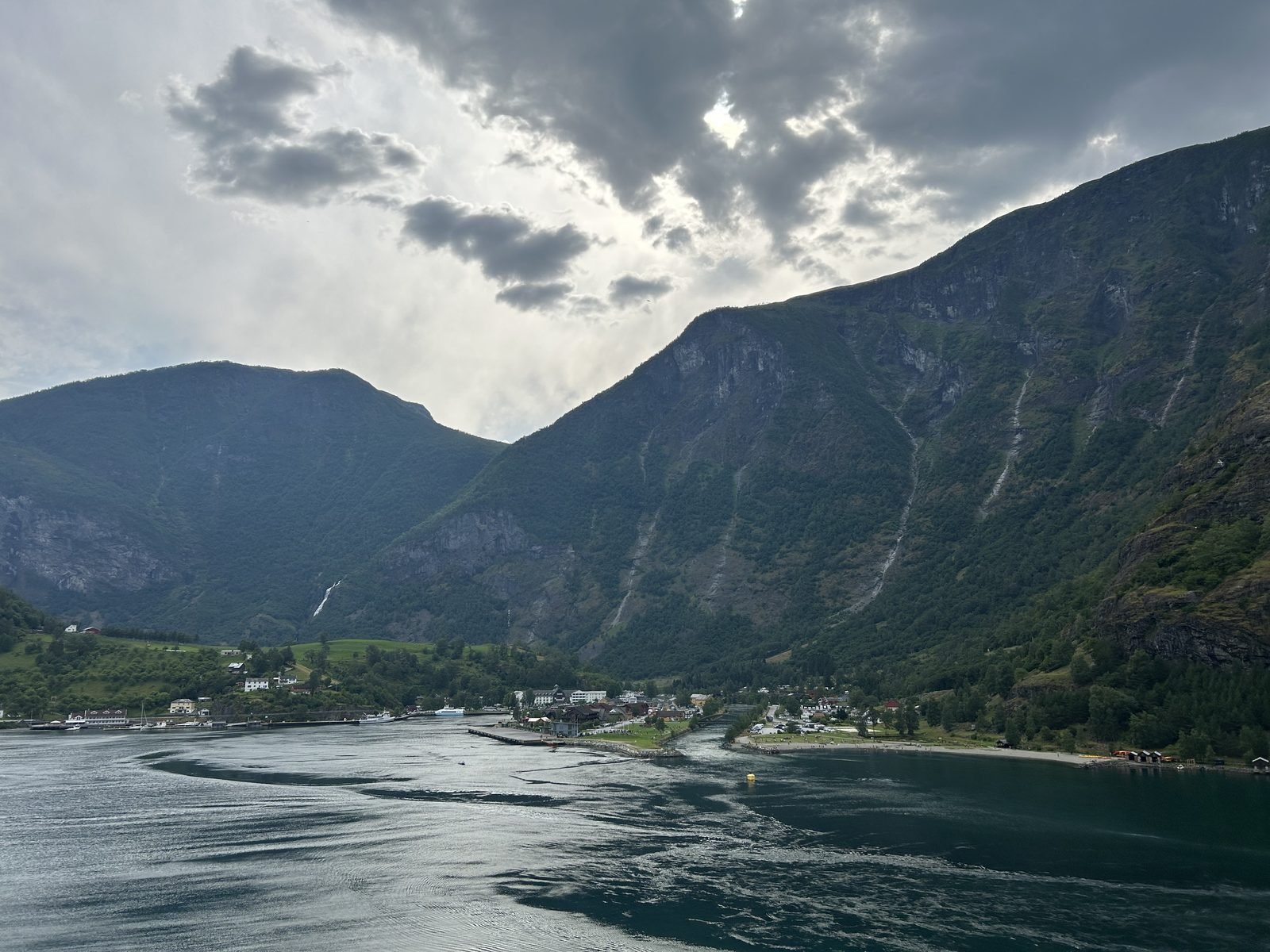 Blick auf das Dorf Flåm am Ende des Aurlandsfjords mit Wasserfällen an den Berghängen, Norwegen