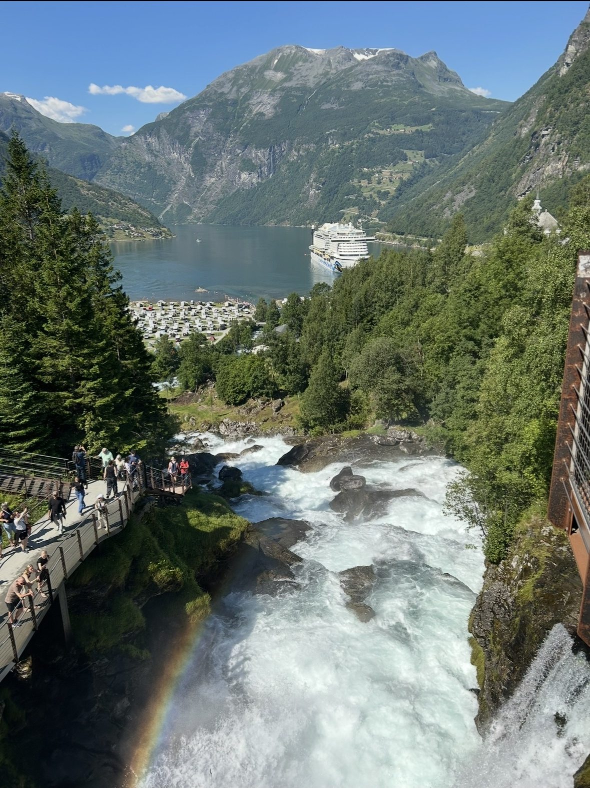 Wasserfall im Geirangerfjord mit Blick auf ein Kreuzfahrtschiff im Fjord, Norwegen